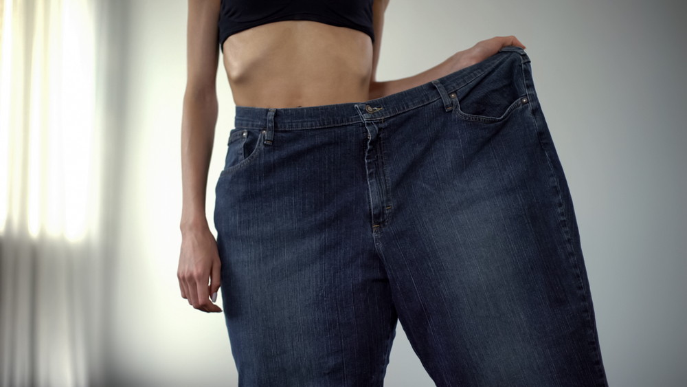 Person standing on a scale with a measuring tape, representing rapid weight loss risks