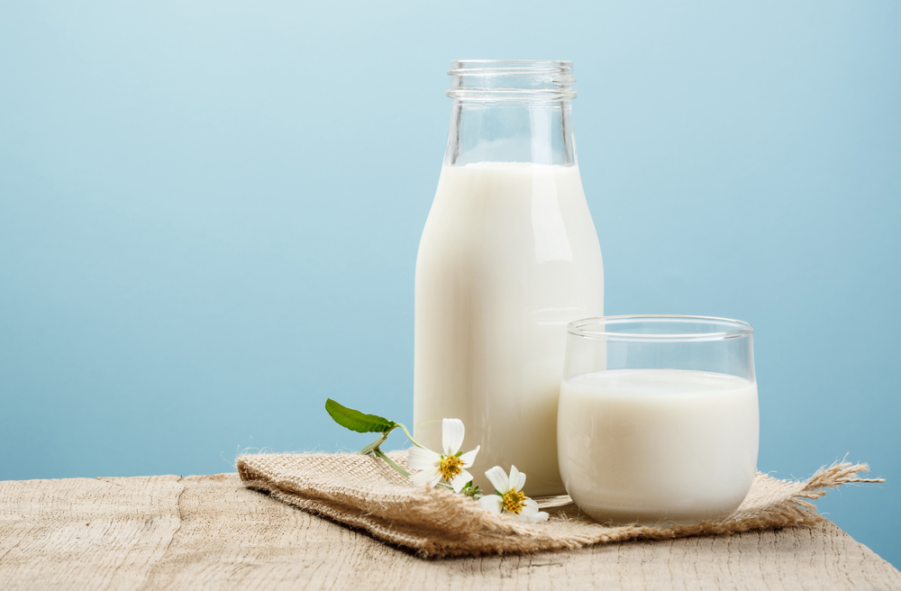 Glass of milk on a table with healthy foods, representing the connection between milk consumption and weight gain.