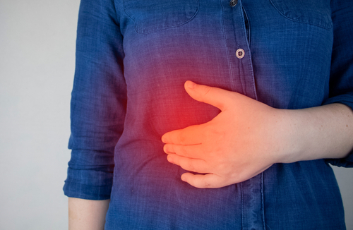 Woman holding her upper abdomen in pain below the ribs, illustrating causes like indigestion, GERD, or gallbladder issues